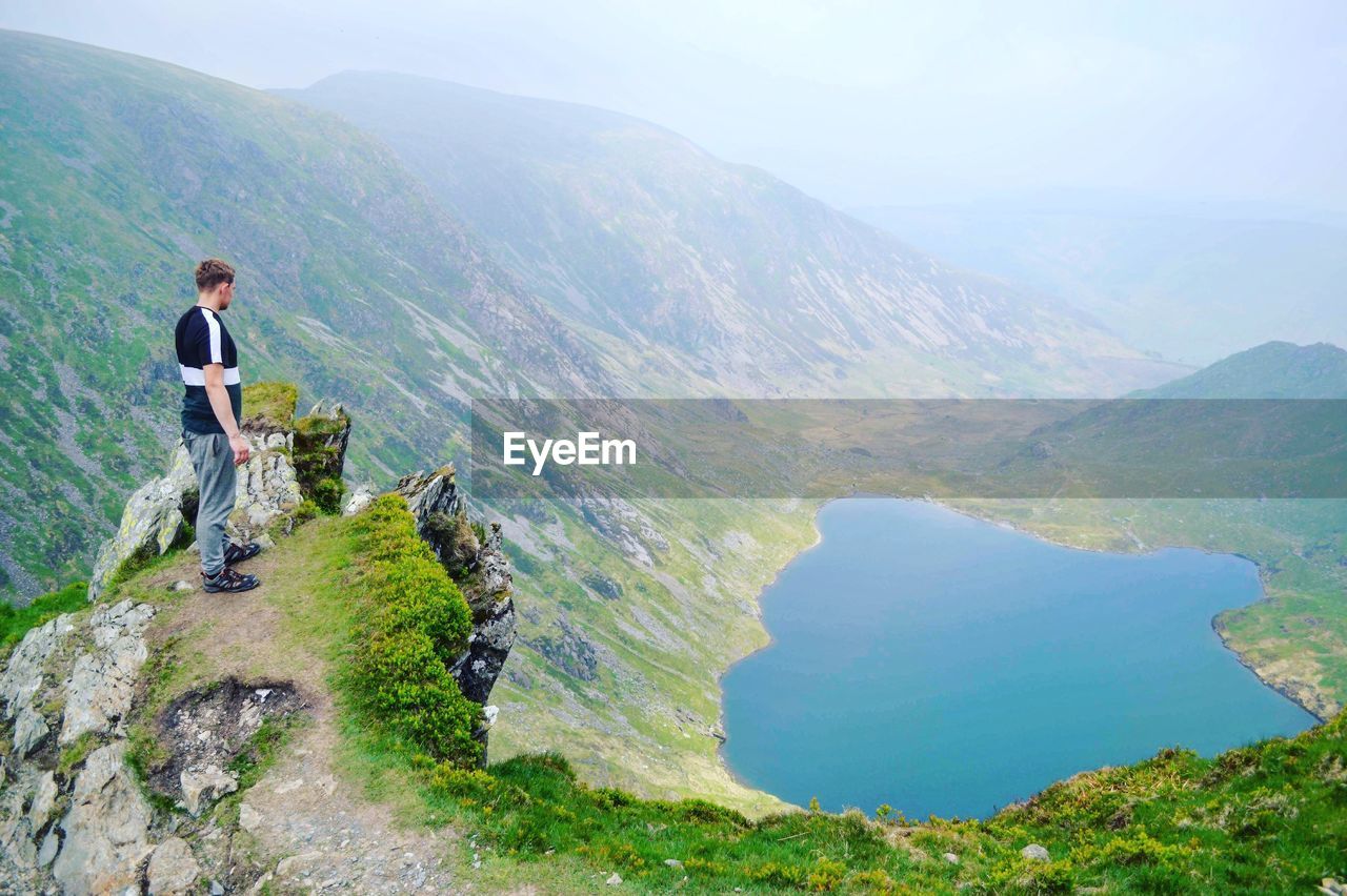 MAN STANDING ON MOUNTAIN AGAINST MOUNTAINS