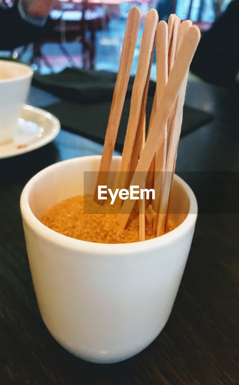 Close-up of brown sugar and wooden sticks in a paper cup for being served with coffee 