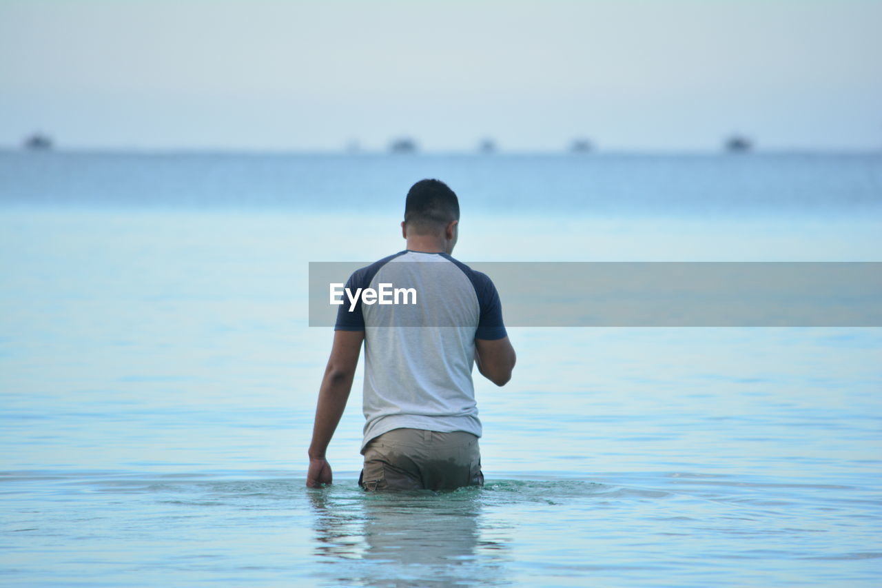 Rear view of man wading in sea against sky