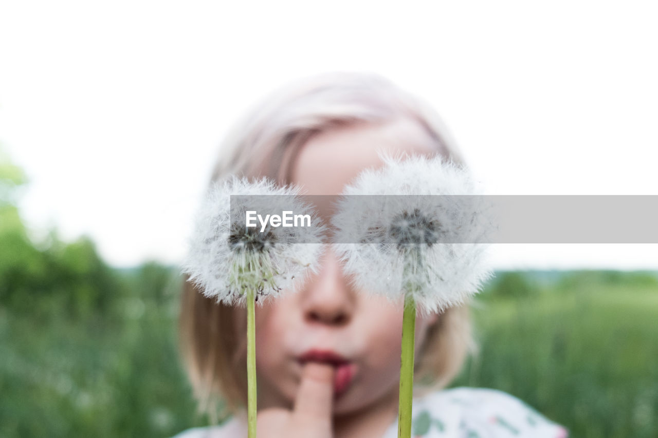 Close-up of cute girl with dandelions against clear sky