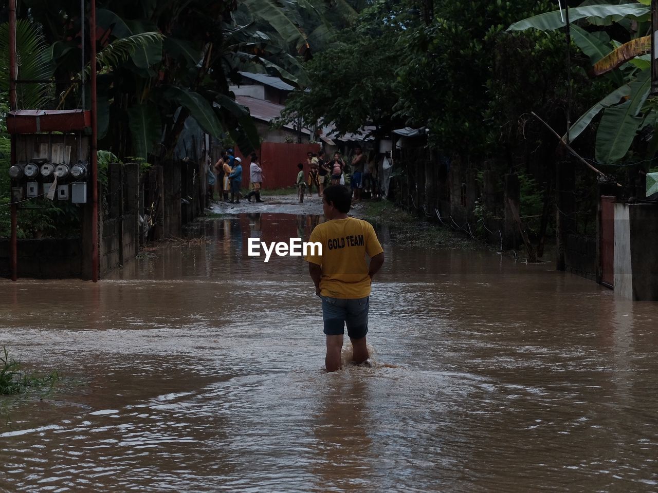 FULL LENGTH REAR VIEW OF MAN STANDING ON WET ROAD