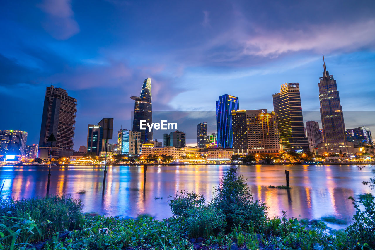 ILLUMINATED BUILDINGS BY RIVER AGAINST SKY