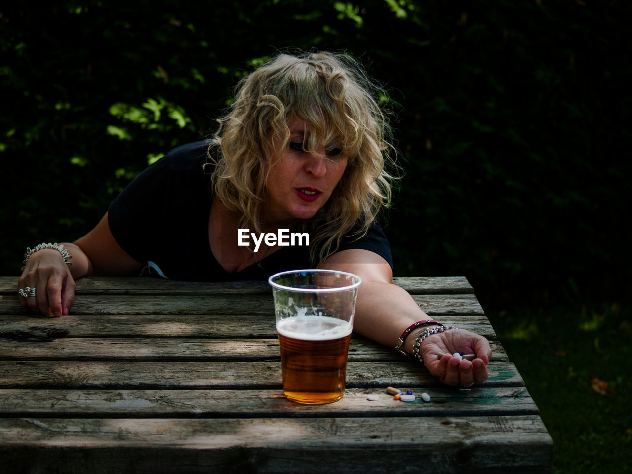 Woman drinking beer while holding pills on table