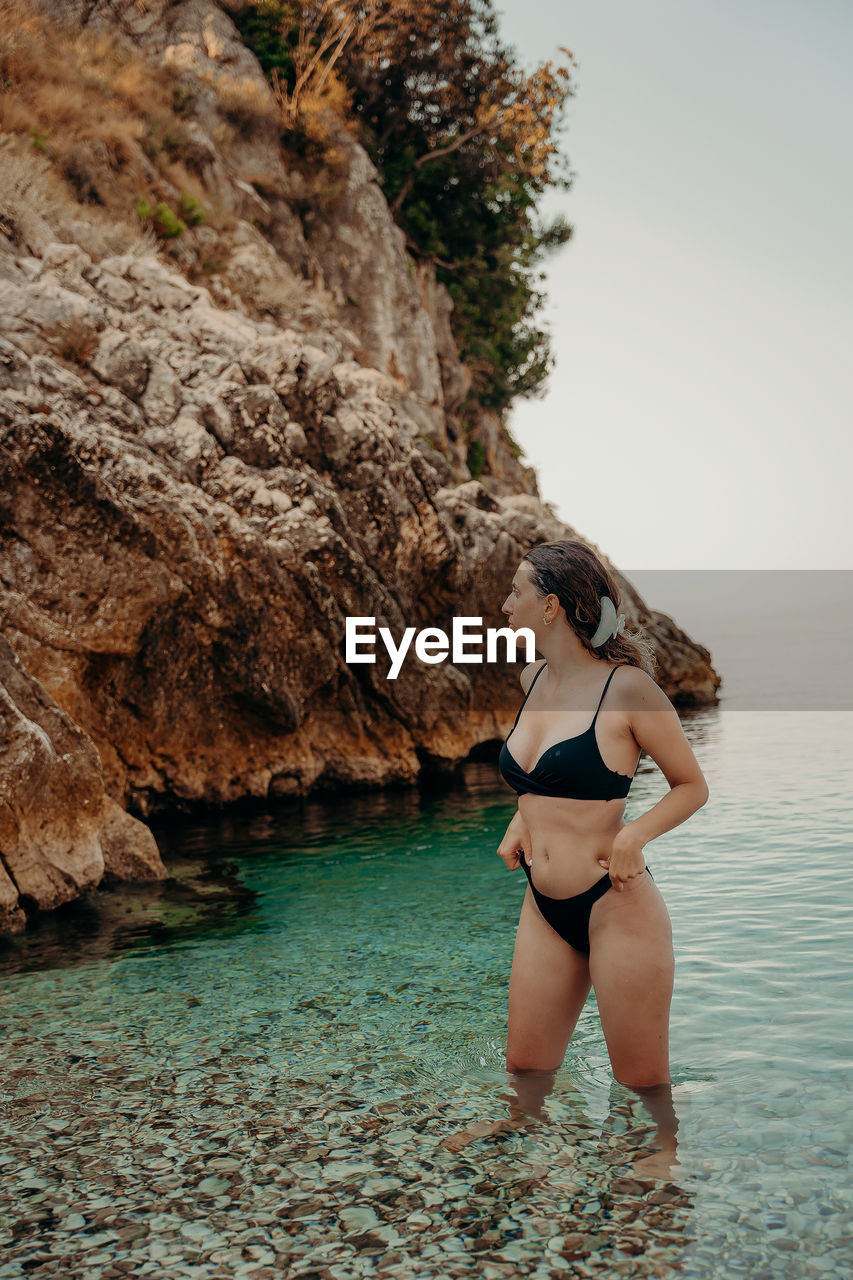 one person, adult, rock, water, sea, swimwear, women, clothing, bikini, young adult, nature, female, land, leisure activity, lifestyles, beach, photo shoot, full length, vacation, human leg, holiday, trip, beauty in nature, limb, swimsuit bottom, rock formation, lingerie, relaxation, standing, day, hairstyle, sports, exercising, outdoors, coast, tranquility, person, undergarment, sky, summer, long hair, sports clothing, travel, fashion, brassiere, scenics - nature, sunlight