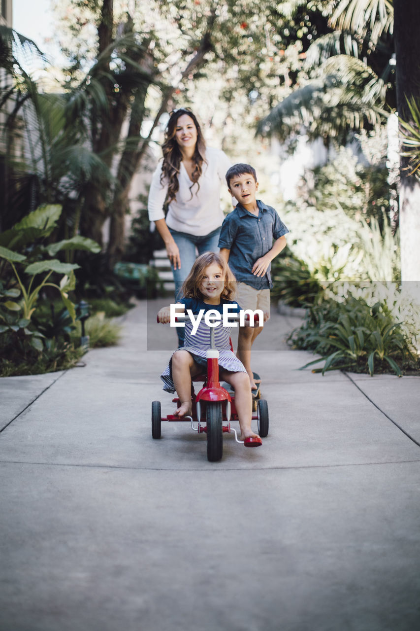 Daughter riding tricycle while mother and brother standing in background