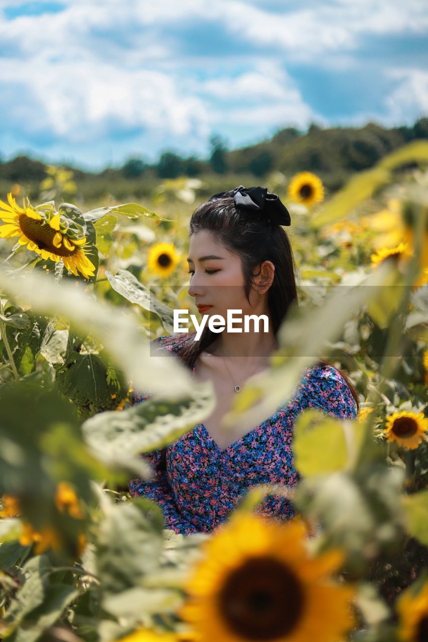 PORTRAIT OF WOMAN ON SUNFLOWER AT FIELD