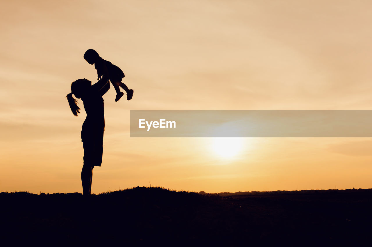 SILHOUETTE MAN STANDING ON FIELD AGAINST ORANGE SKY