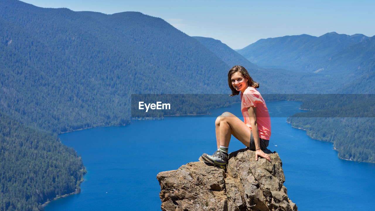 Hiker girl is on top of the mountain overlooking deep blue lake