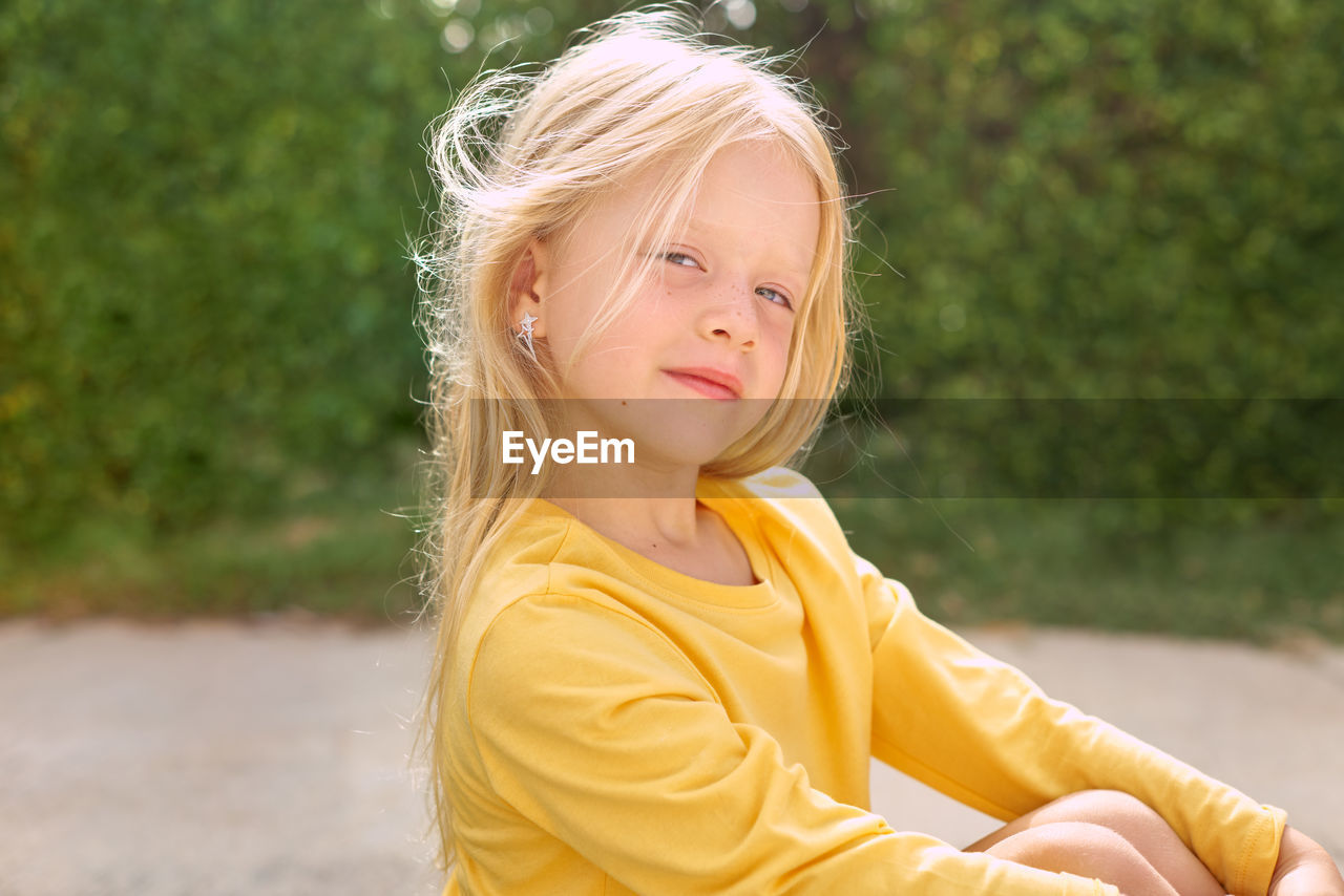 Portrait of young pretty girl sitting against green plants 