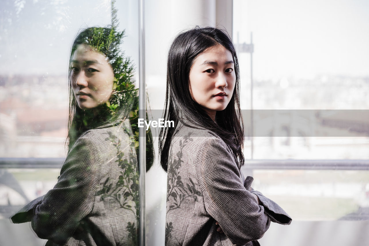 Portrait of confident chinese business woman with arms crossed in office. reflection on glass