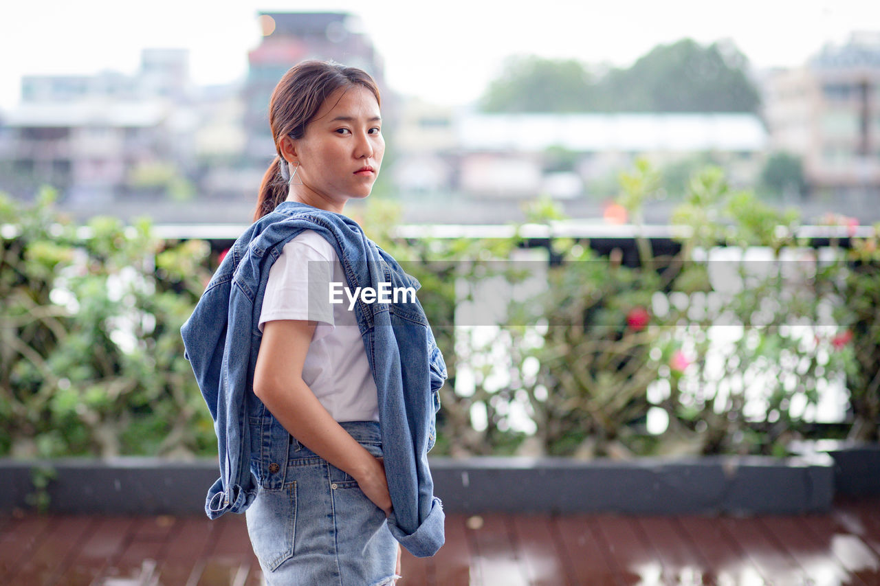 Portrait of young woman standing against city in background