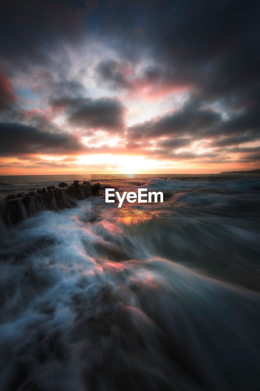 Scenic view of sea against dramatic sky during sunset