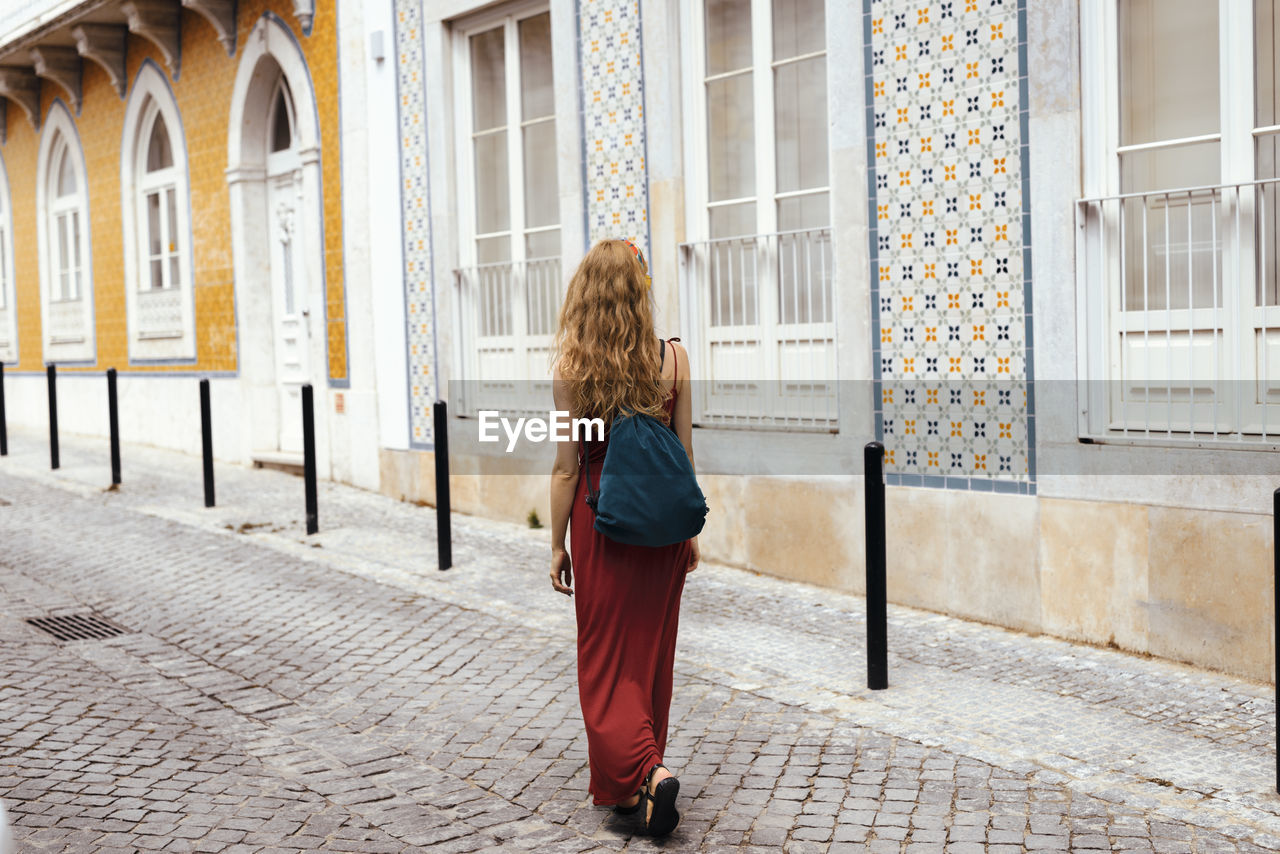 Rear view of woman with backpack walking on footpath amidst buildings