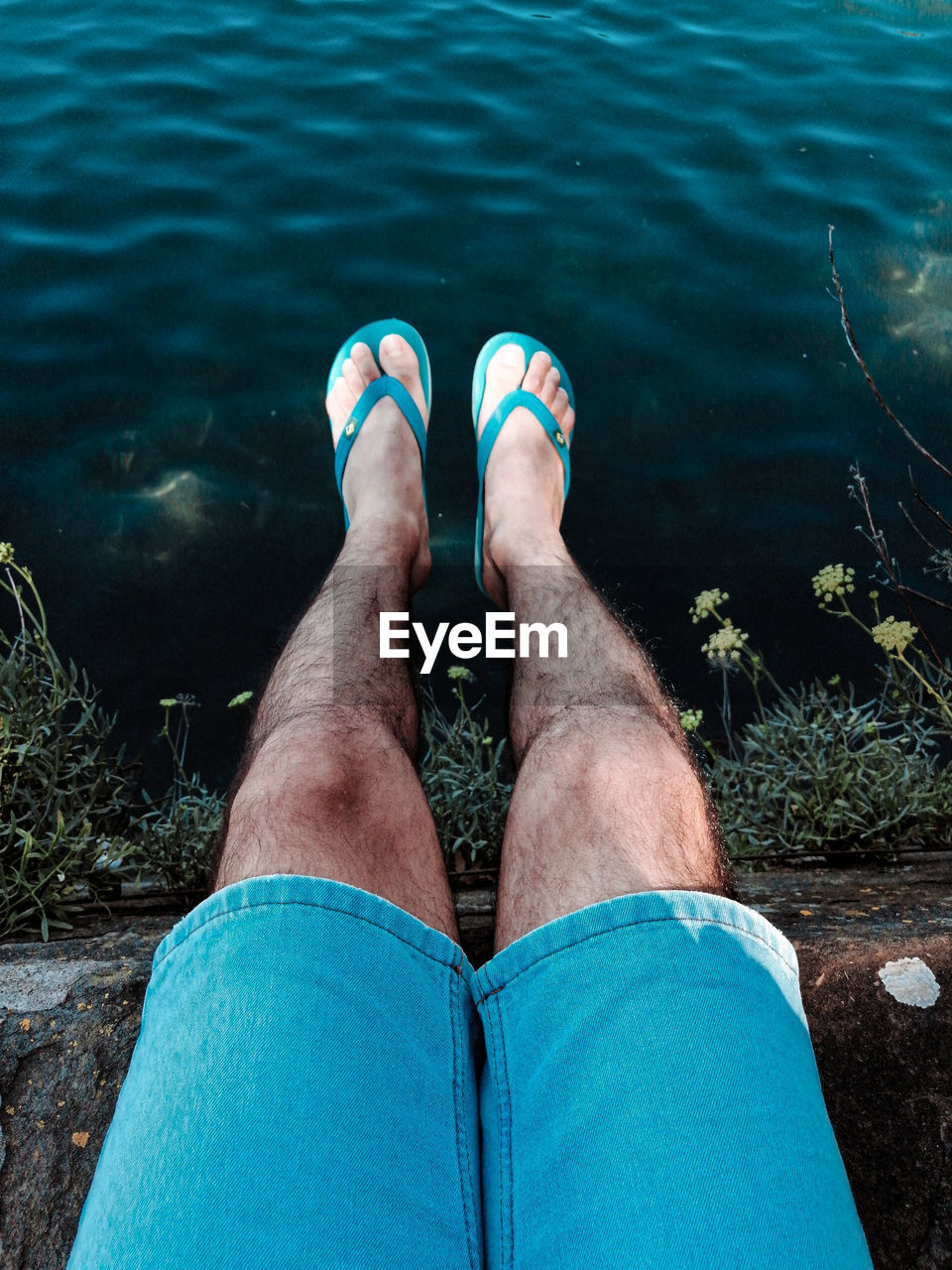 Low section of man relaxing by lake