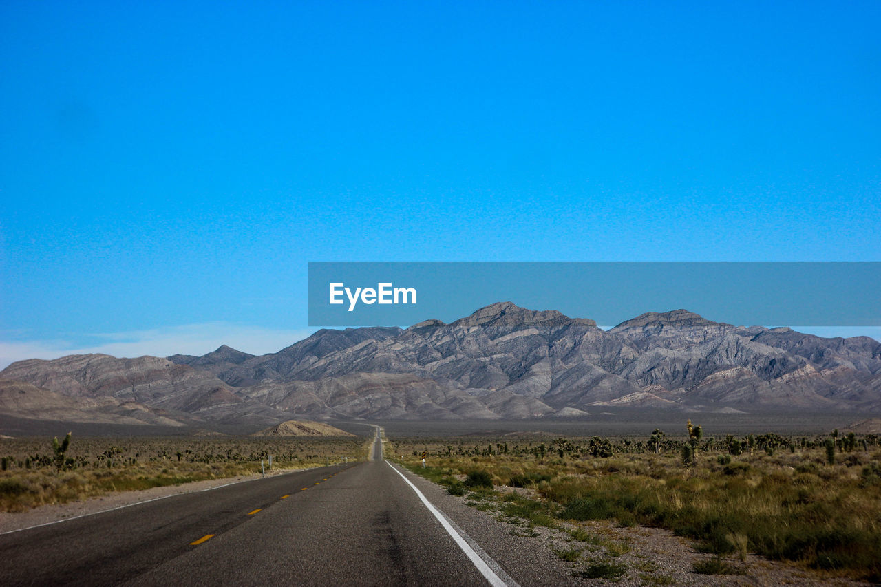 Road amidst desert against clear blue sky