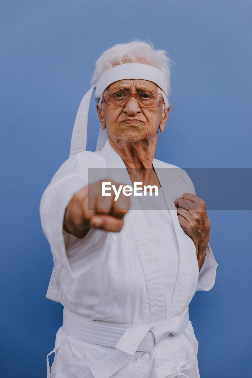 Portrait of senior woman doing karate against blue background