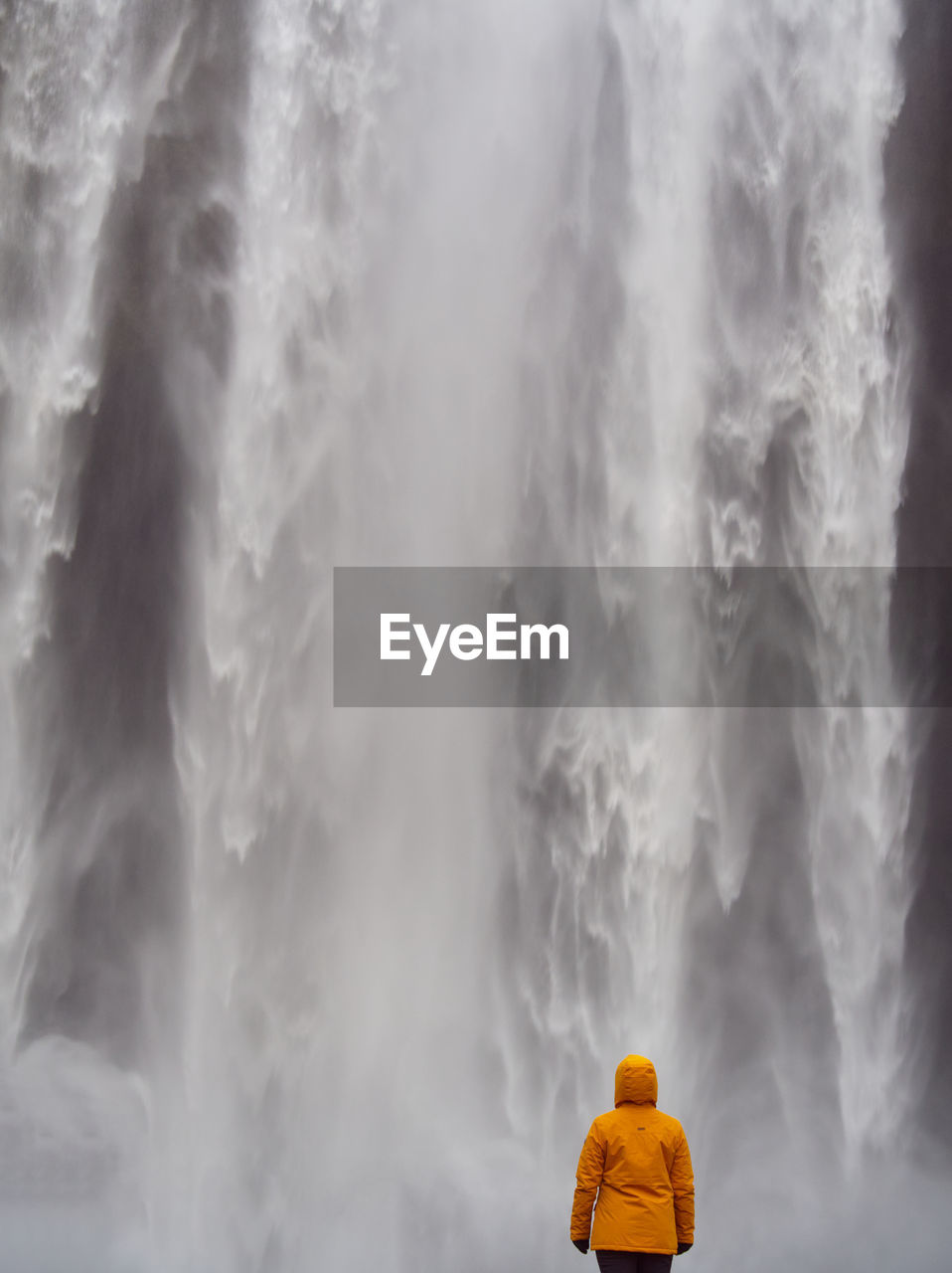 Rear view of man standing against yellow waterfall