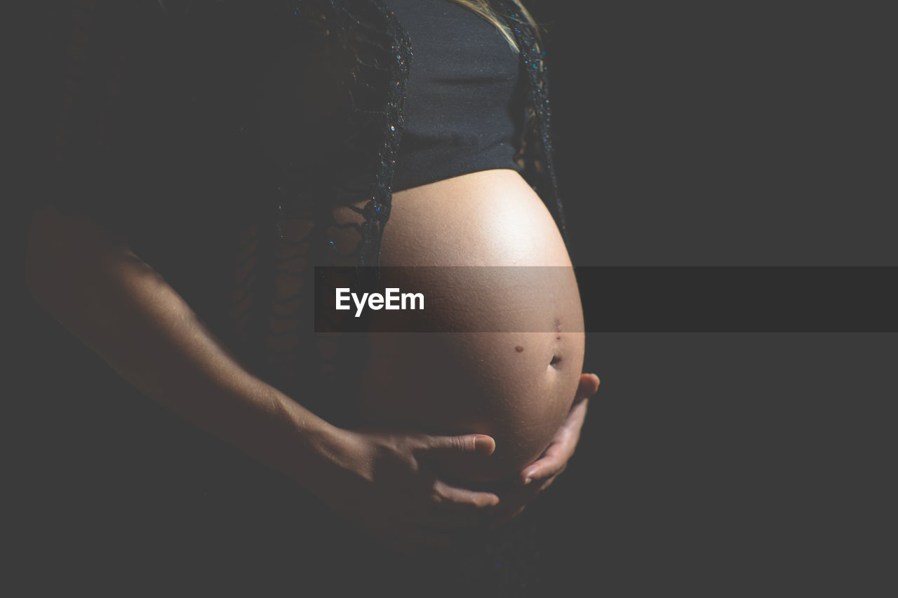 Midsection of pregnant woman against black background