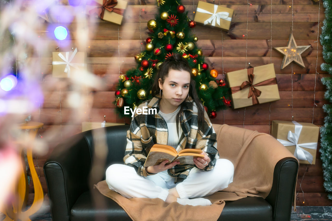 A young girl is reading a book comfortably sitting the sofa on new year's eve.