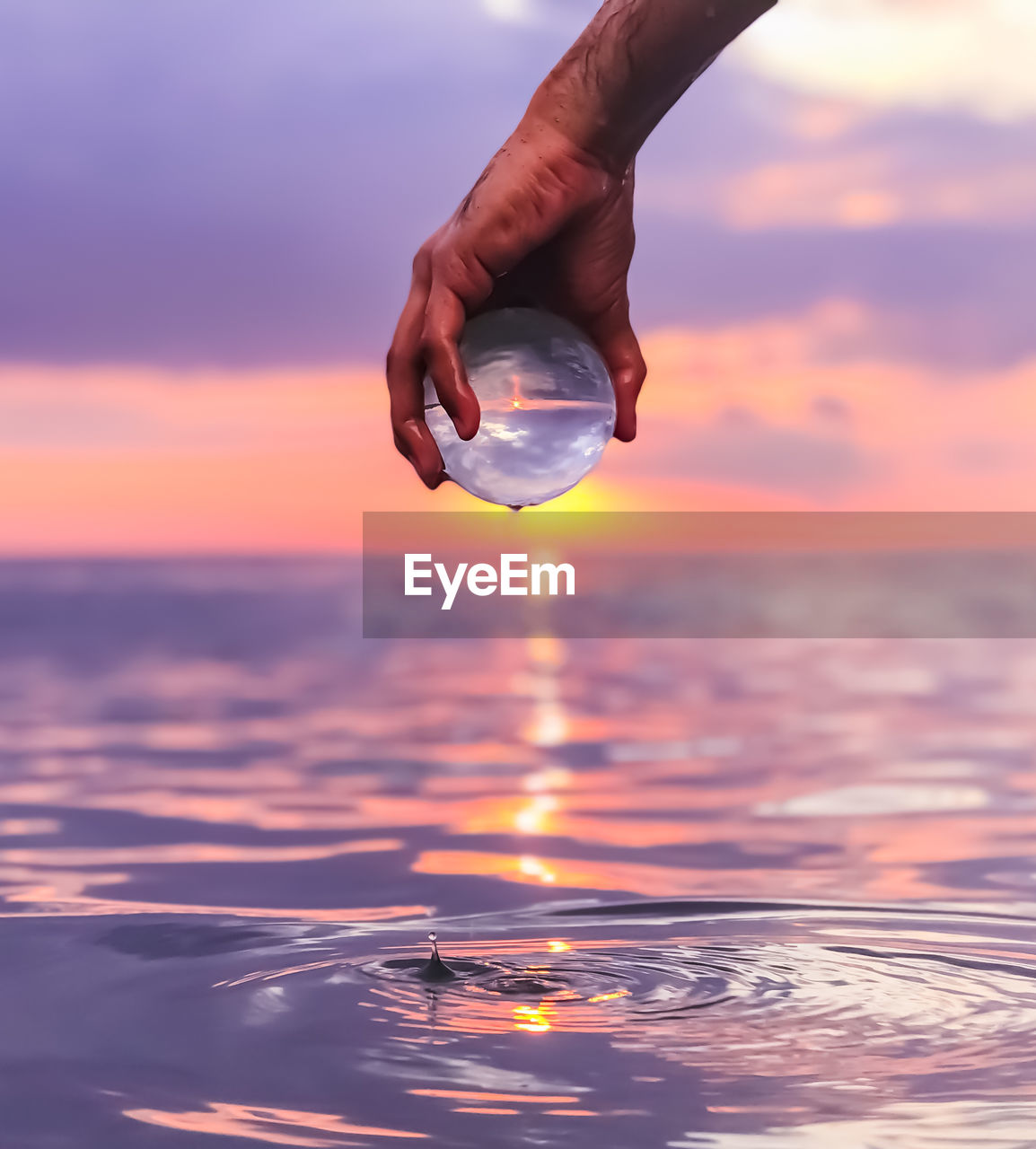 Close-up of hand holding crystal ball at beach during sunset