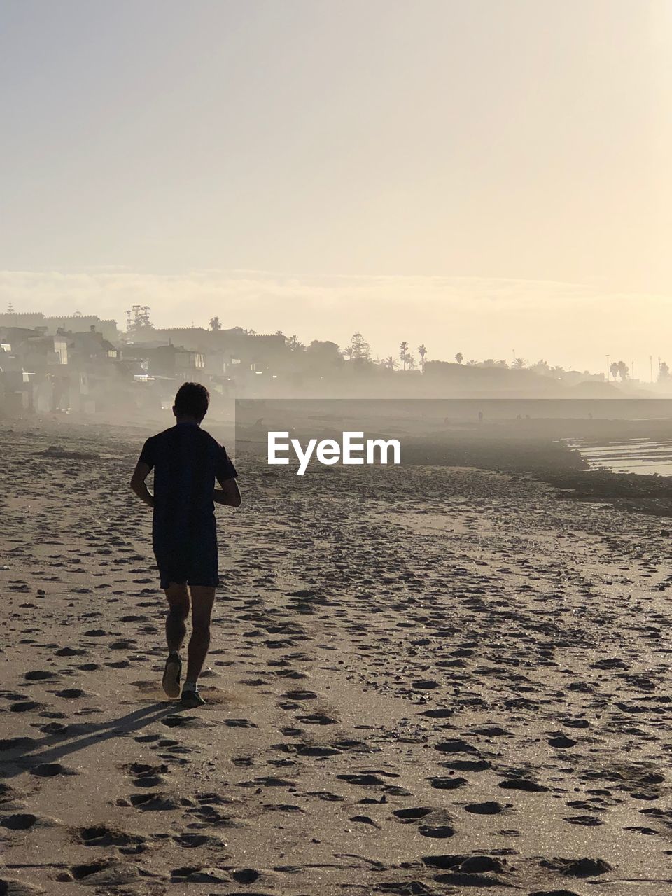 REAR VIEW OF MAN AT BEACH DURING SUNSET