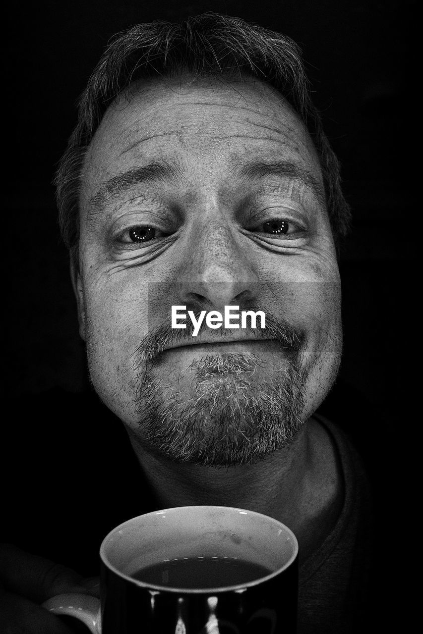 Close-up portrait of man holding coffee cup against black background