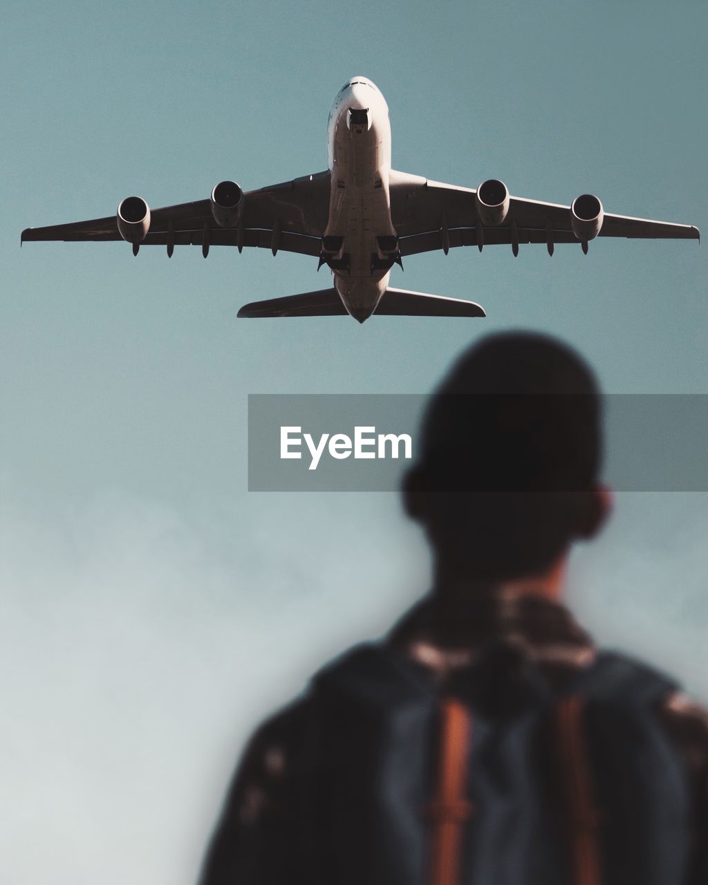 Rear view of person looking at airplane flying in sky