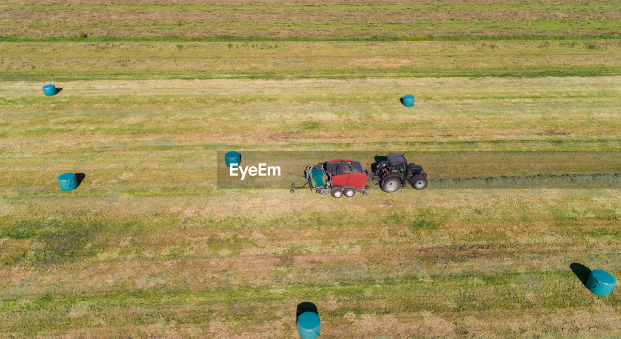 Black tractor with a red straw chamber press during the straw harvest on a mown field