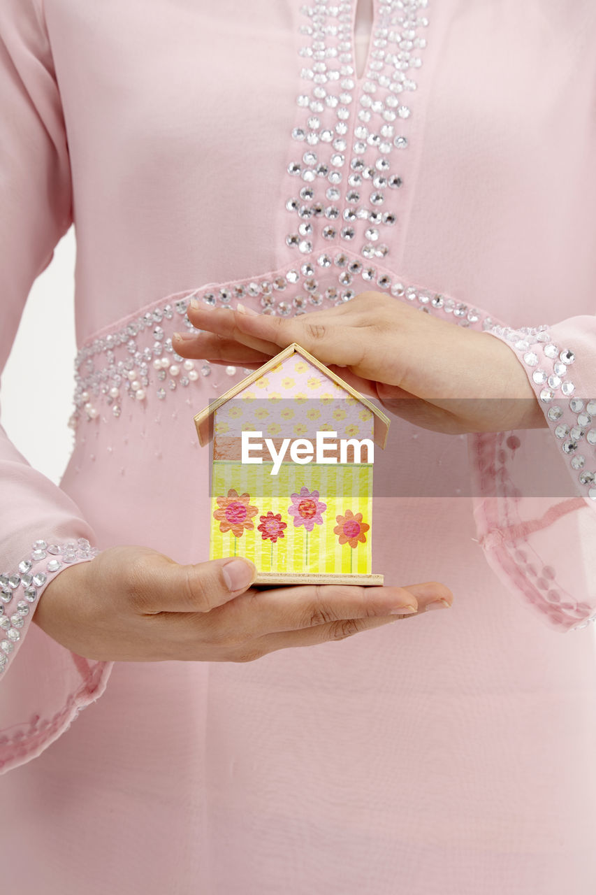 Midsection of woman holding model home against white background