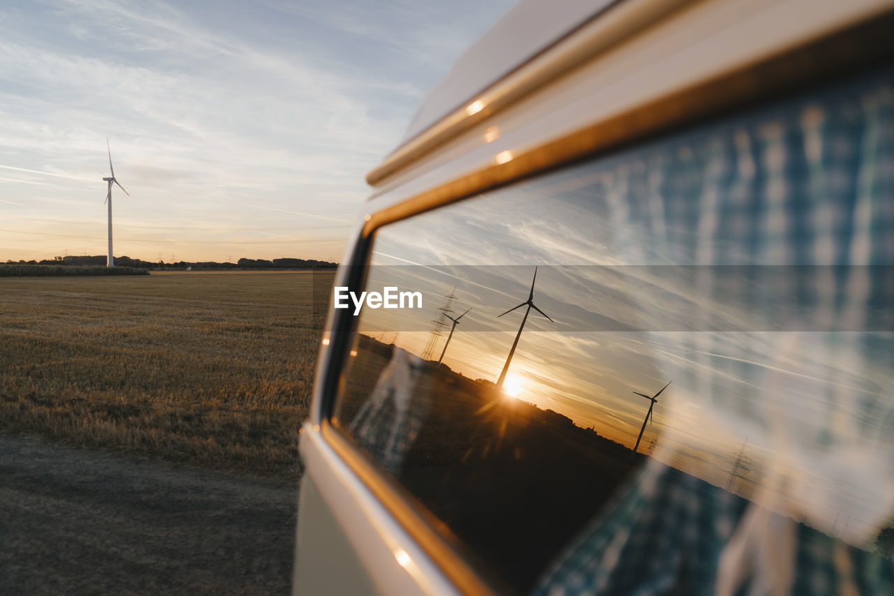 Camper van in rural landscape with wind turbines at sunset