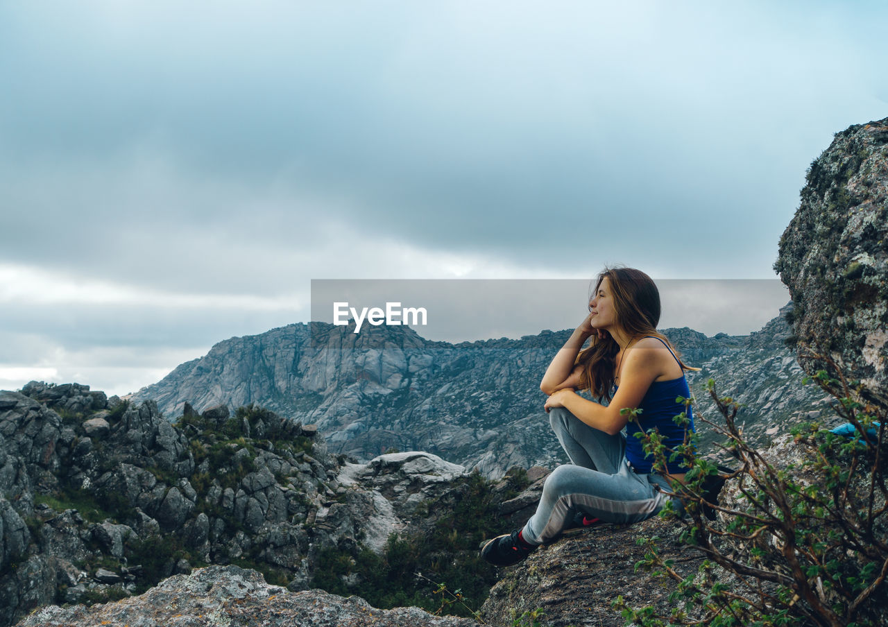 Smiling woman sitting on rock against mountain