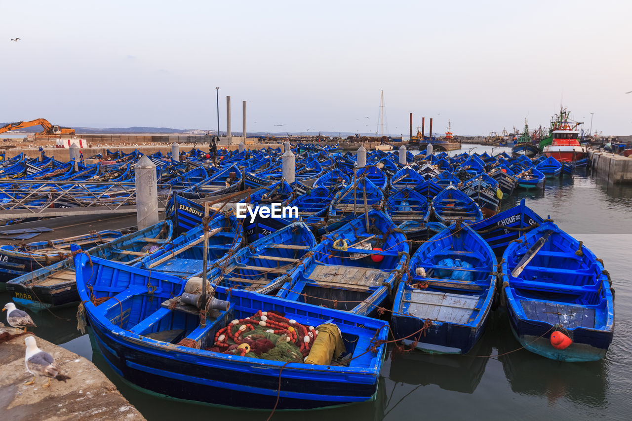 BOATS MOORED AT HARBOR AGAINST BLUE SKY