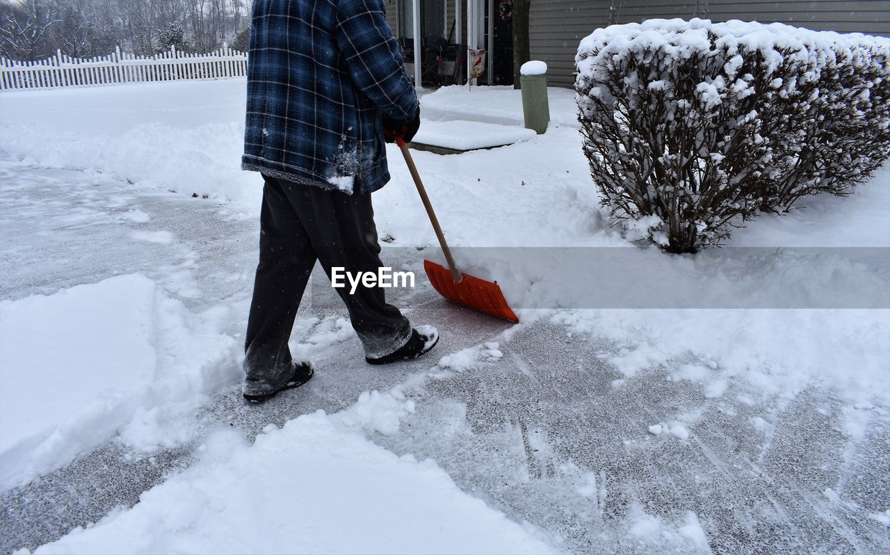 Low section of man cleaning on snow covered yard