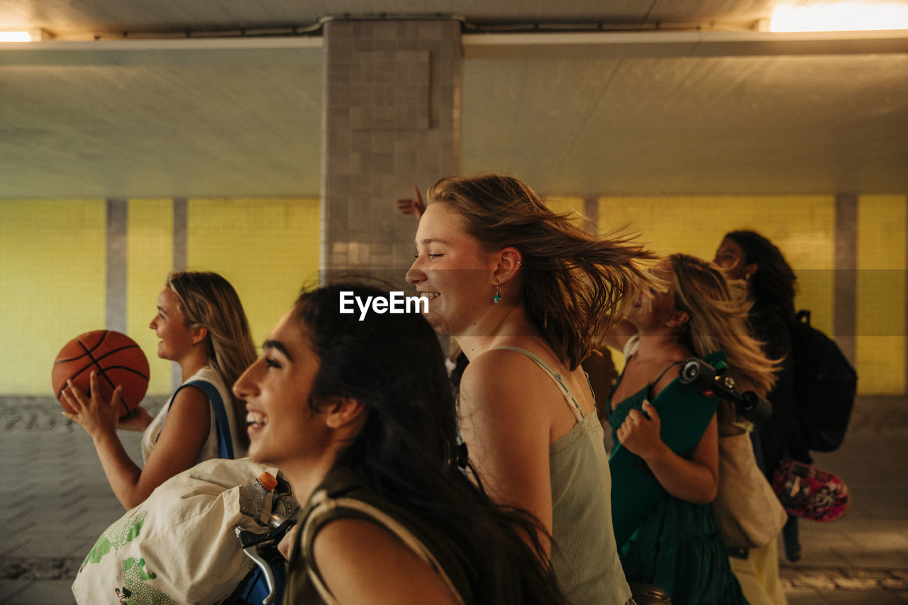 Smiling teenage girl with tousled hair walking with friends under bridge