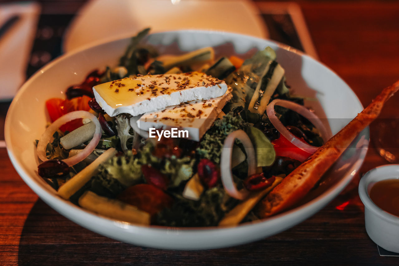 Close up healthy vegetable salad with a large piece of cheese, olive oil onion and spices.