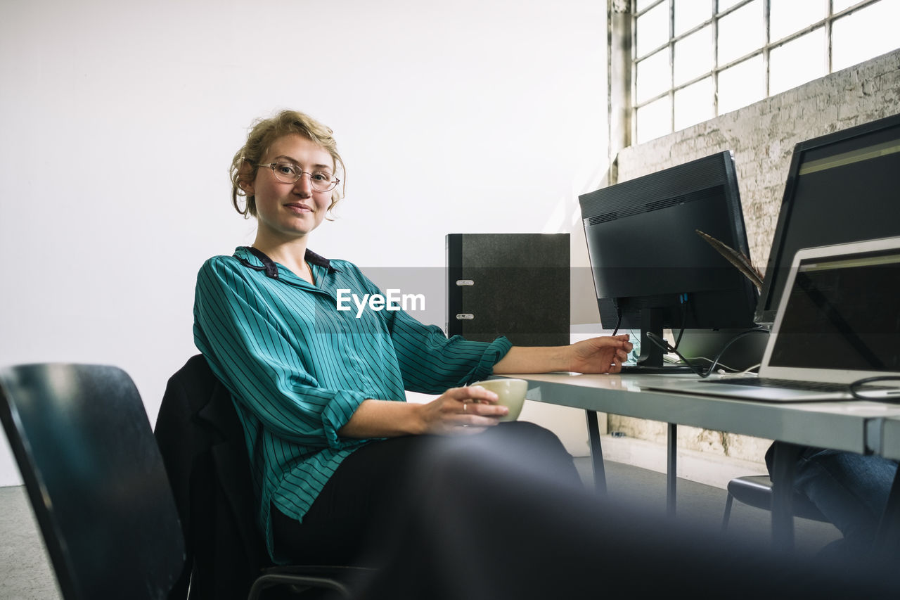 Portrait of confident young businesswoman sitting at desk in creative office