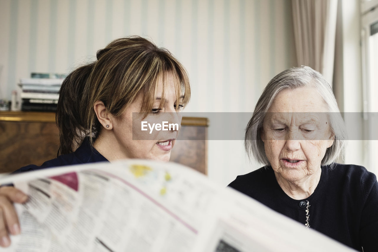Caretaker with senior woman reading newspaper at nursing home