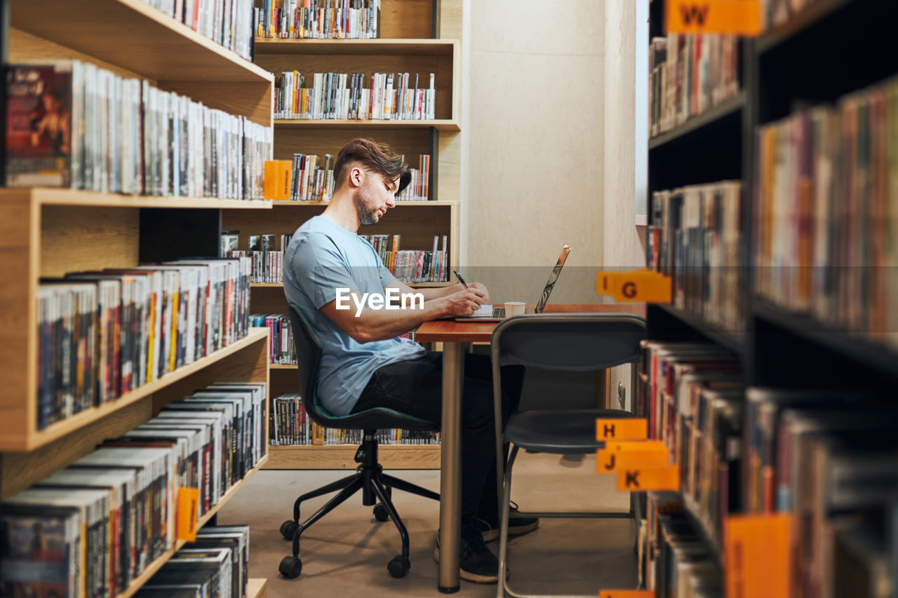 Student learning in library. young man preparing for test on laptop. man listening to online course