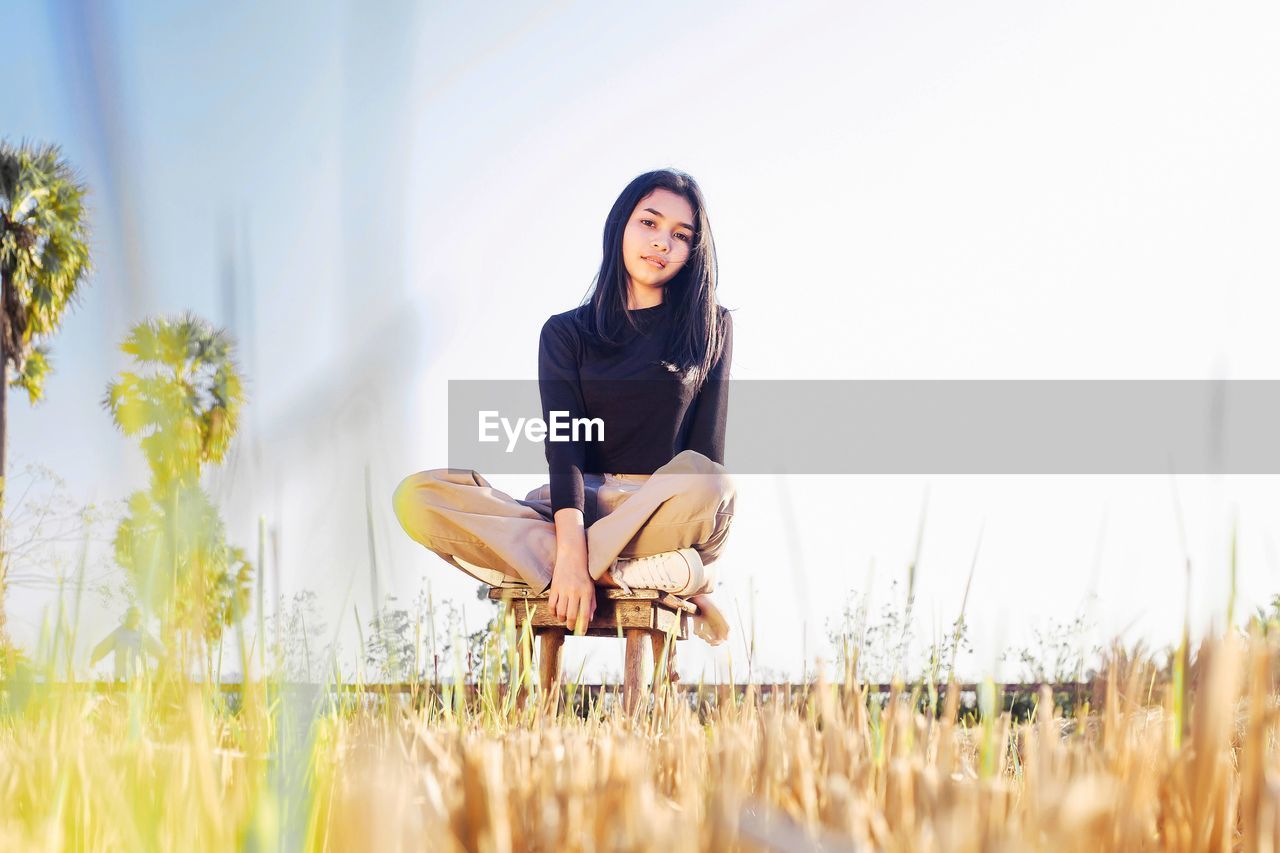 Portrait of smiling young woman sitting on field against sky