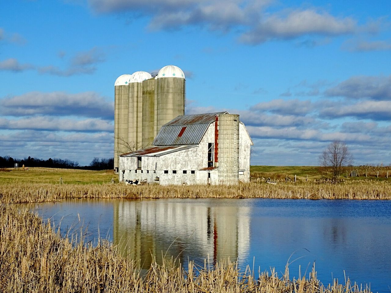 Old barn and silo on field by lake against sky