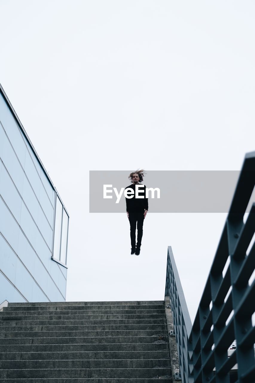 LOW ANGLE VIEW OF PERSON ON STAIRCASE AGAINST BUILDINGS