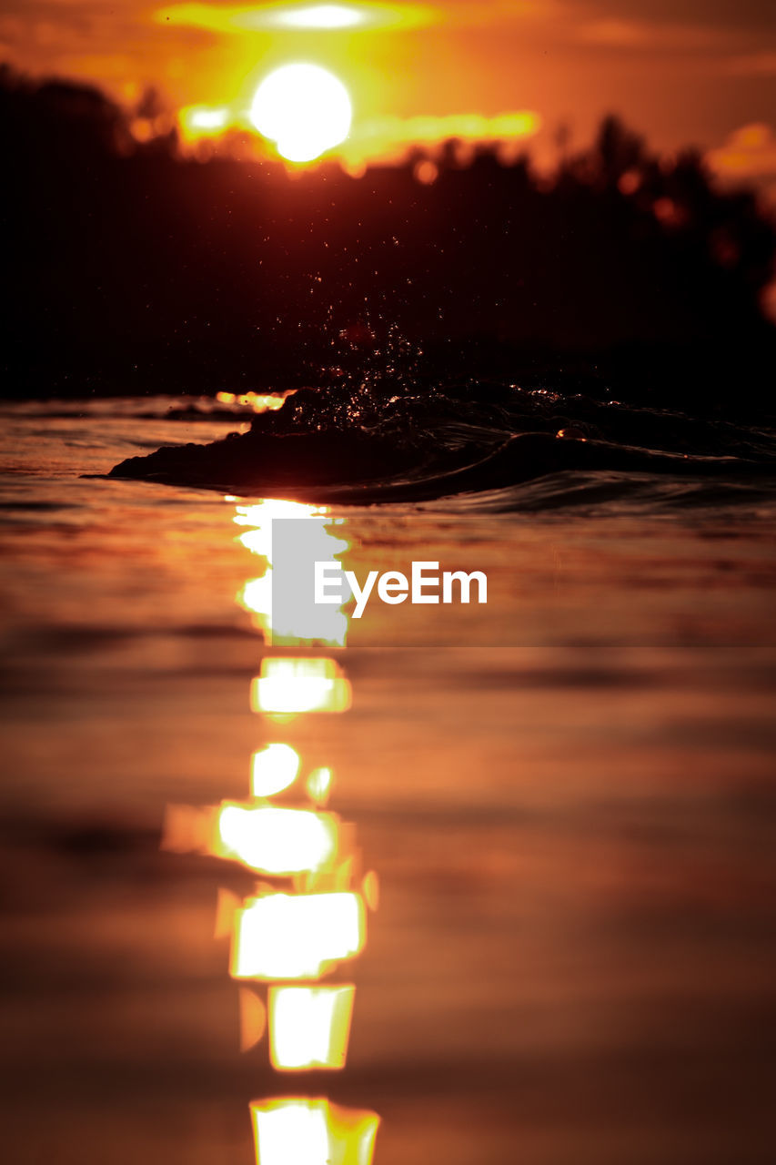 CLOSE-UP OF ILLUMINATED WATER AGAINST ORANGE SKY