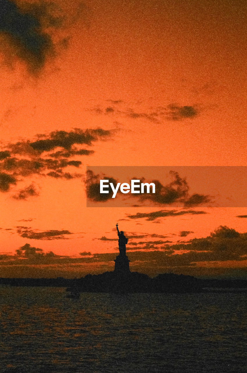Silhouette statue of liberty by bay of water during sunset