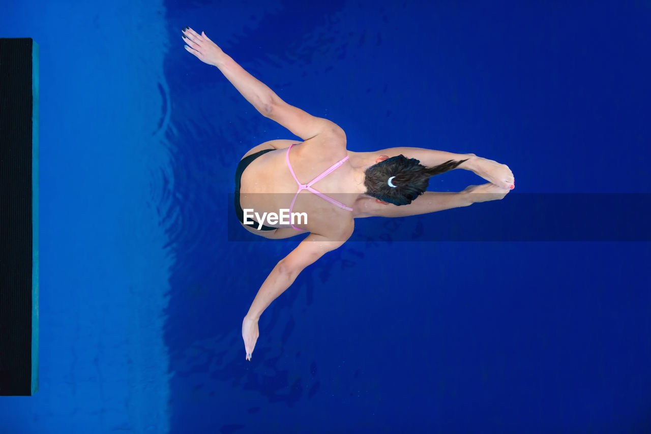 High angle view of woman with arms outstretched diving into swimming pool