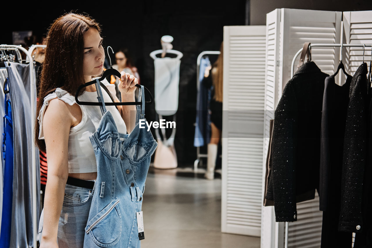 Young brunette latina attractive woman shopper choosing new jeans cloth at store.