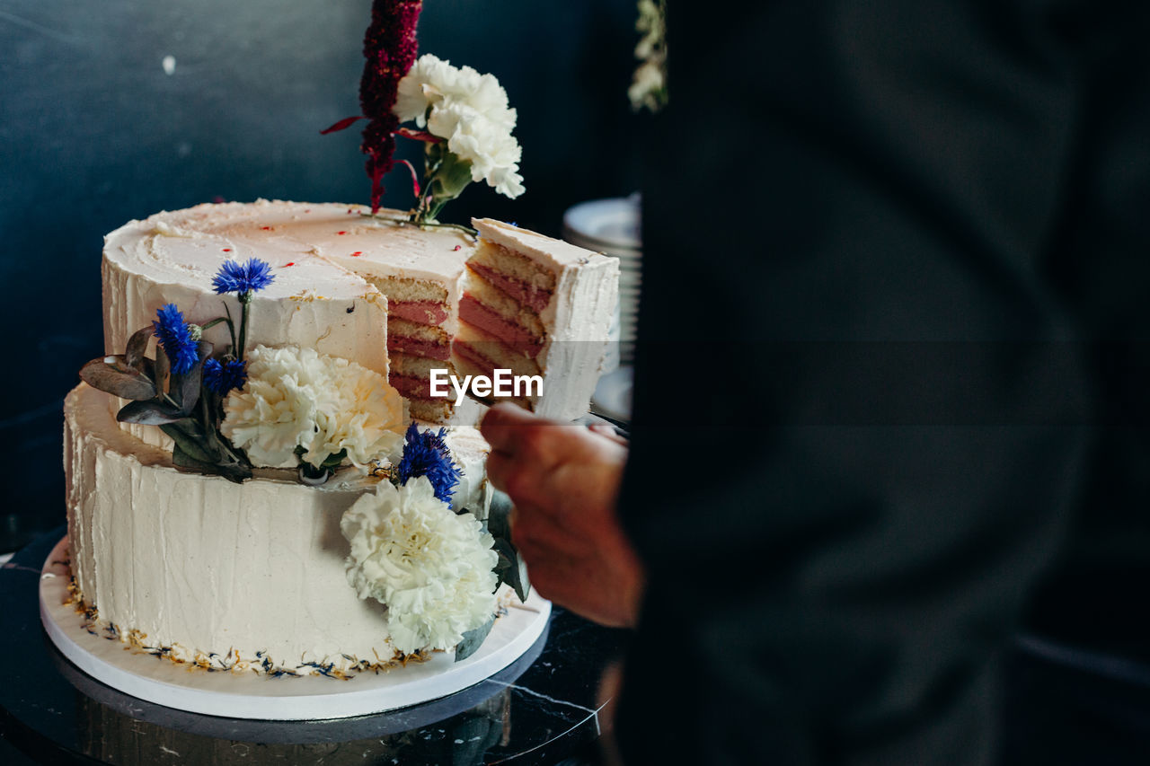 Midsection of man taking cake slice at wedding ceremony