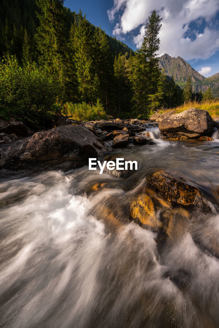 SCENIC VIEW OF STREAM FLOWING THROUGH ROCKS IN MOUNTAINS