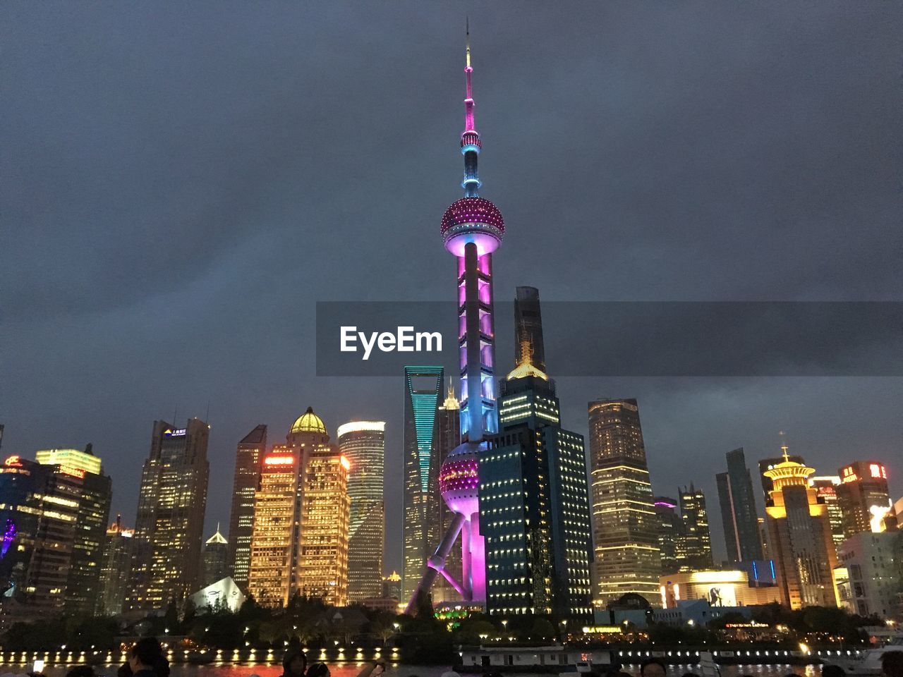 Low angle view of illuminated oriental pearl tower amidst buildings in city at dusk