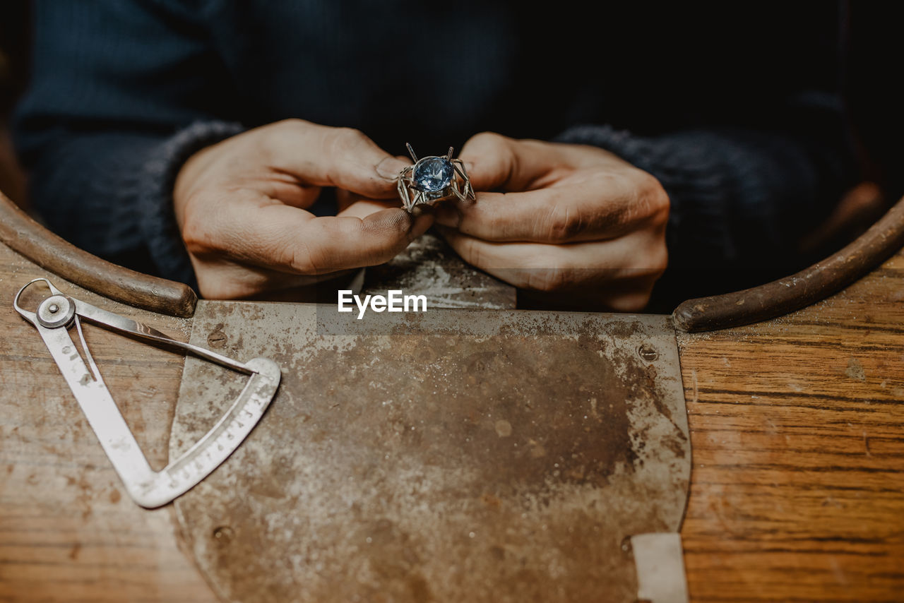 Anonymous jeweler holding unfinished ring in dirty hands and checking quality in workshop