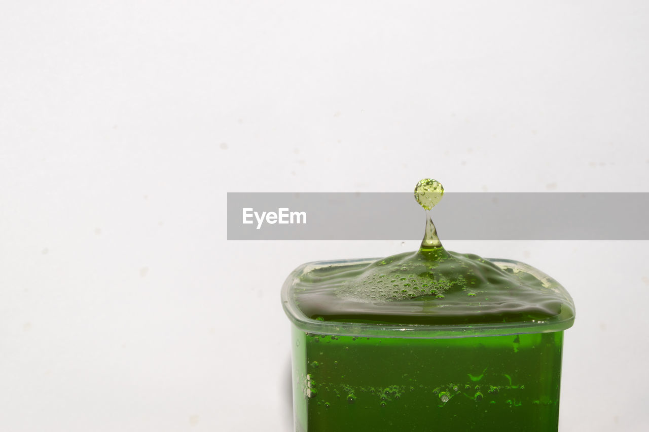 Close-up of splashing droplet in drink against white background